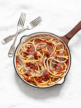 Traditional italian roman pasta - bucatini with amatricana tomato sauce in a cooking pan on a light background, top view