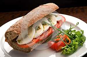 Traditional Italian sandwich with mozzarella, fresh tomatoes and pesto on a white plate