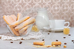 Traditional italian savoiardi or ladyfingers biscuits in a glass bowl and pieces of cookies and sugar on the table