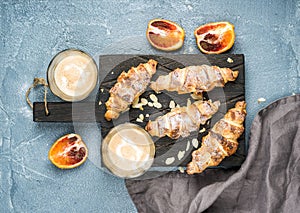 Traditional Italian style home breakfast. Latte in glasses, almond croissants and red bloody Sicilian oranges over