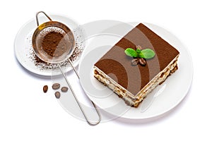 Traditional Italian Tiramisu square dessert portion on ceramic plate and strainer with cocoa powder isolated on white