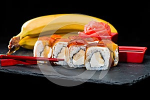 Traditional Japanese cuisine. Sweet sushi rolls with salmon, cream cheese, rice and banana was poured with jam on dark background