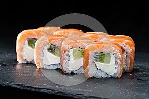 Traditional Japanese cuisine. Sweet sushi rolls with salmon, cream cheese, rice and kiwi on dark background, selective focus