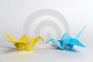 Traditional Japanese origami cranes made of blue and yellow paper on a white background. Pair of colorful paper birds