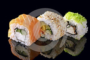 Traditional Japanese sushi rolls on a black background with a reflection of three pieces