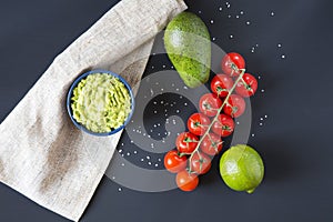 Traditional latinamerican mexican sauce guacamole in ceramic bowl and ingredients on dark background.