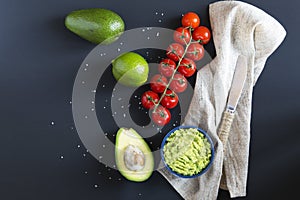 Traditional latinamerican mexican sauce guacamole in ceramic bowl and ingredients on dark background.