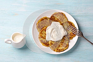 Traditional latkes fritters with sour cream on light blue textured background
