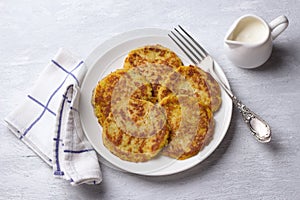 Traditional latkes fritters with sour cream on a light gray textured background