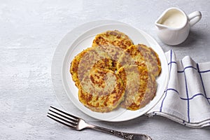 Traditional latkes fritters with sour cream on a light gray textured background