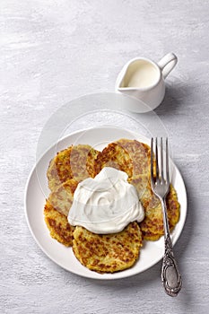 Traditional latkes fritters with sour cream on a light gray textured background