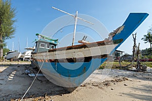Traditional long tail fishing boat in need of repair moored in the sand