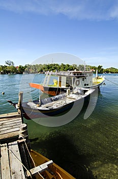 Traditional malaysian fisherman boat moored, wooden jetty and blue sky background