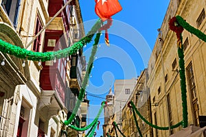 Traditional Maltese limestone buildings with hanging decorations around coloured balconies in the old city Birgu, Citta Vittoriosa