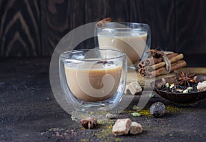 Traditional masala chai in glass cup with ingredients cinnamon, anise, cardamom, nutmeg, pepper and brown sugar.