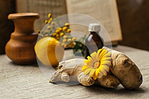 Traditional medicine background with ginger and calendula at blurred vintage recipy book, lemon, wooden jug, pharmacy bottle,