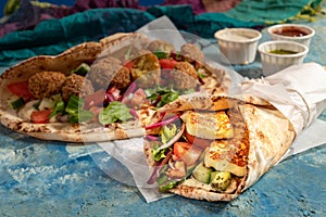 Traditional Mediterranean Arabic grilled halloumi and falafel, hummus and vegetables in flatbread wraps with herbs and sauces