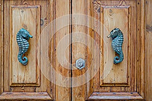 Traditional metal seahorse door handle on wooden door, Malta
