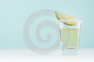 Traditional mexican alcohol drink - tequila in elegant shot glass with salt rim and green lime slice in modern pastel mint.
