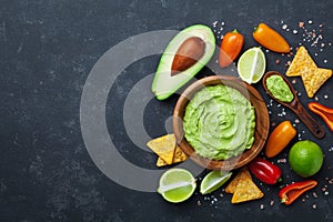 Traditional mexican food. Bowl guacamole sauce with avocado, lime and nachos on black table top view. Copy space for recipe.