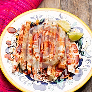 Mexican jicama  cutted with chili powder and piquant sauce on wooden background