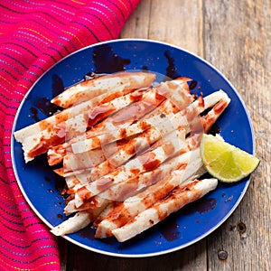 Mexican jicama  cutted with chili powder and piquant sauce on wooden background