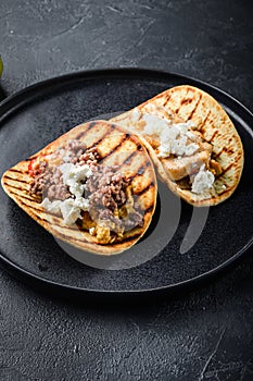 Traditional mexican taco with chicken and beef with ingredients a side on black plate over black textured background side view,