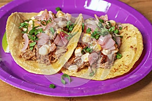 Traditional Mexican tacos with meat and vegetables in purple paper plates served for takeaway on wood table.