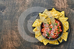 Traditional Mexican tomato sauce salsa with nachos and ingredients tomatoes, chile, garlic, onion on dark old wooden background.