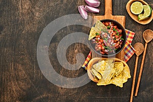 Traditional Mexican tomato sauce salsa with nachos and ingredients tomatoes, chile, garlic, onion on dark old wooden background.