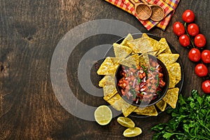 Traditional Mexican tomato sauce salsa with nachos and ingredients tomatoes, chile, garlic, onion on dark old wooden background.