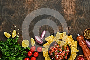 Traditional Mexican tomato sauce salsa with nachos and ingredients tomatoes, chile, garlic, onion on dark old wooden background.