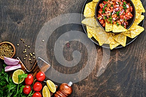 Traditional Mexican tomato sauce salsa with nachos and ingredients tomatoes, chile, garlic, onion on dark old wooden background.