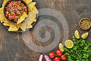 Traditional Mexican tomato sauce salsa with nachos and ingredients tomatoes, chile, garlic, onion on dark old wooden background. C photo