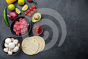 Traditional mexican tortilla with a mix of ingredients, corn, meat, vegetables, salsa, sauce over black textured background, top