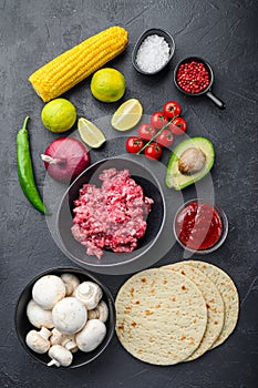 Traditional mexican tortilla with a mix of ingredients, corn, meat, vegetables, salsa, sauce over black textured background, top