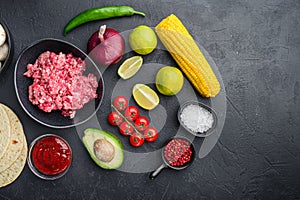 Traditional mexican tortilla with a mix of ingredients, corn, meat, vegetables, salsa, sauce over black textured background, top