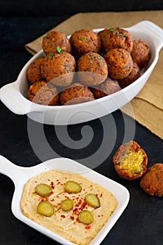 Traditional Middle Eastern food, Falafel (tamiya) with hummus and pickles on black wooden background and yellow table cloth.