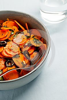 Traditional Moroccan cooked carrot salad North African vegan dish with chopped parsley and olives on gray plate close-up