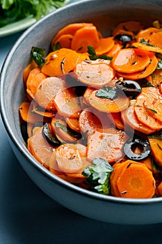 Traditional Moroccan cooked carrot salad North African vegan dish with chopped parsley and olives on gray plate close-up