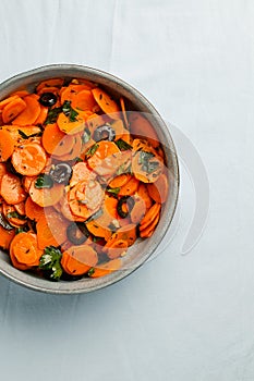 Traditional Moroccan cooked carrot salad North African vegan dish with chopped parsley and olives on gray plate top view