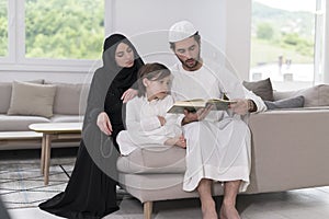 Traditional muslim family parents with children reading Quran and praying together on the sofa before iftar dinner