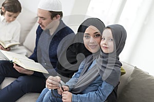 Traditional muslim family parents with children reading Quran and praying together on the sofa before iftar dinner