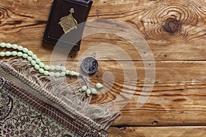 Traditional muslim prayer set bundle. Praying carpet, rosary beads, little version of the Holy Quran and qibla compass on wooden