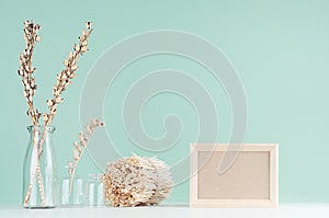 Traditional natural beige home decorations - dry flowers in transparent glass vases, twigs bunch, blank frame on green mint menthe