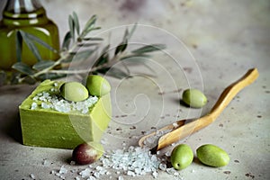 Traditional natural organic olive soap. Close up of handmade soap bar, green olives and leaves and wooden spoon of sea solt on