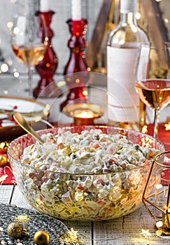 Traditional New Year salad Olivier in bowl on wooden table served with plates, glasses, bottle of wine, candles, garland, festive