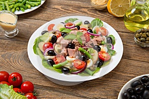 Traditional Nicoise salad in a white plate on an old rural table with sauce and ingredients. Selected focus.