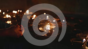 Traditional oil lamps lit at Buddhist temple on Vesak night. Flames flicker, hand ignites new lamps, enlightenment