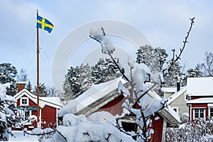 Traditional old big red wooden house in countryside. Snowy village. Beautiful cottage or villa. The flag of Sweden